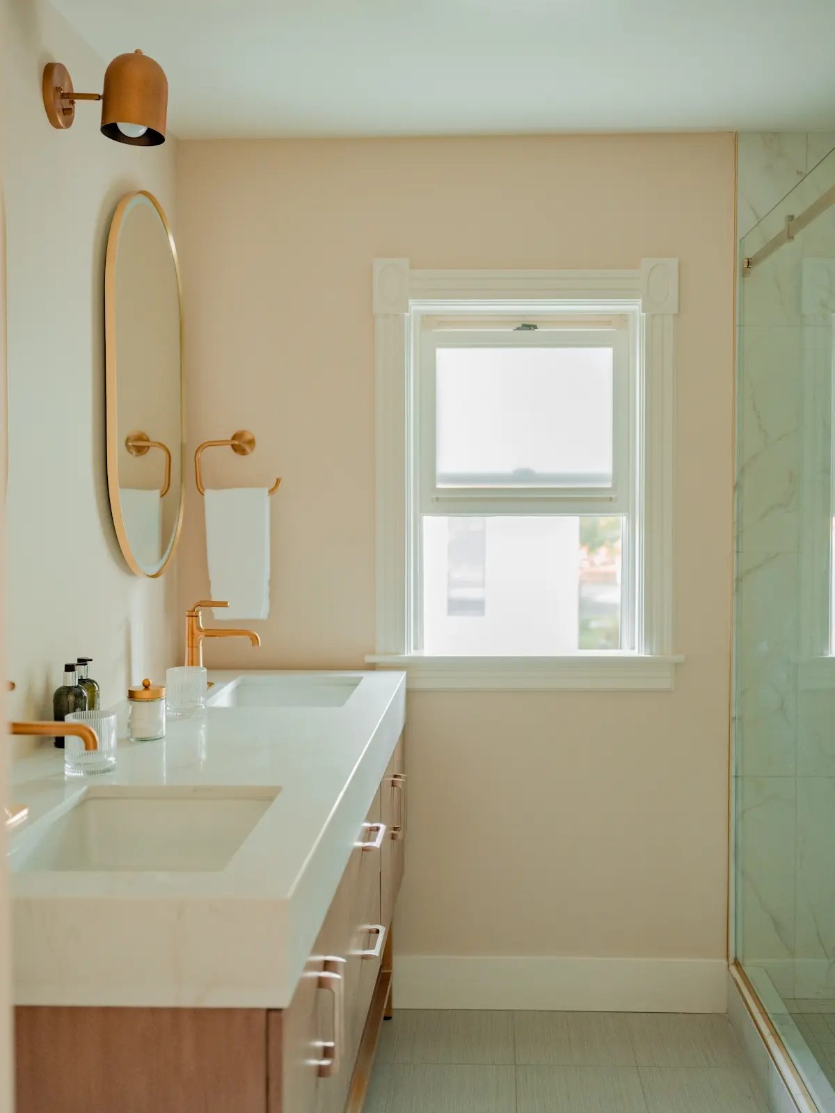 Bathroom with a long vanity, brass fixtures, and an oval mirror.