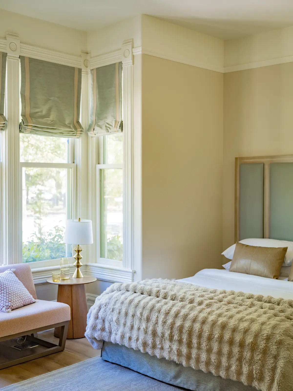 Guest bedroom with a tall upholstered headboard and a chair by the bay windows.