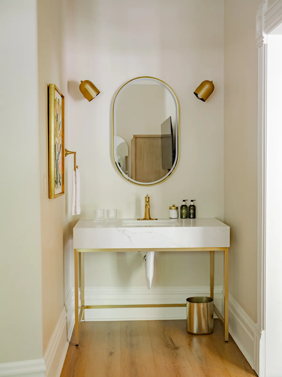 White bathroom vanity with brass fixtures and an oval mirror.