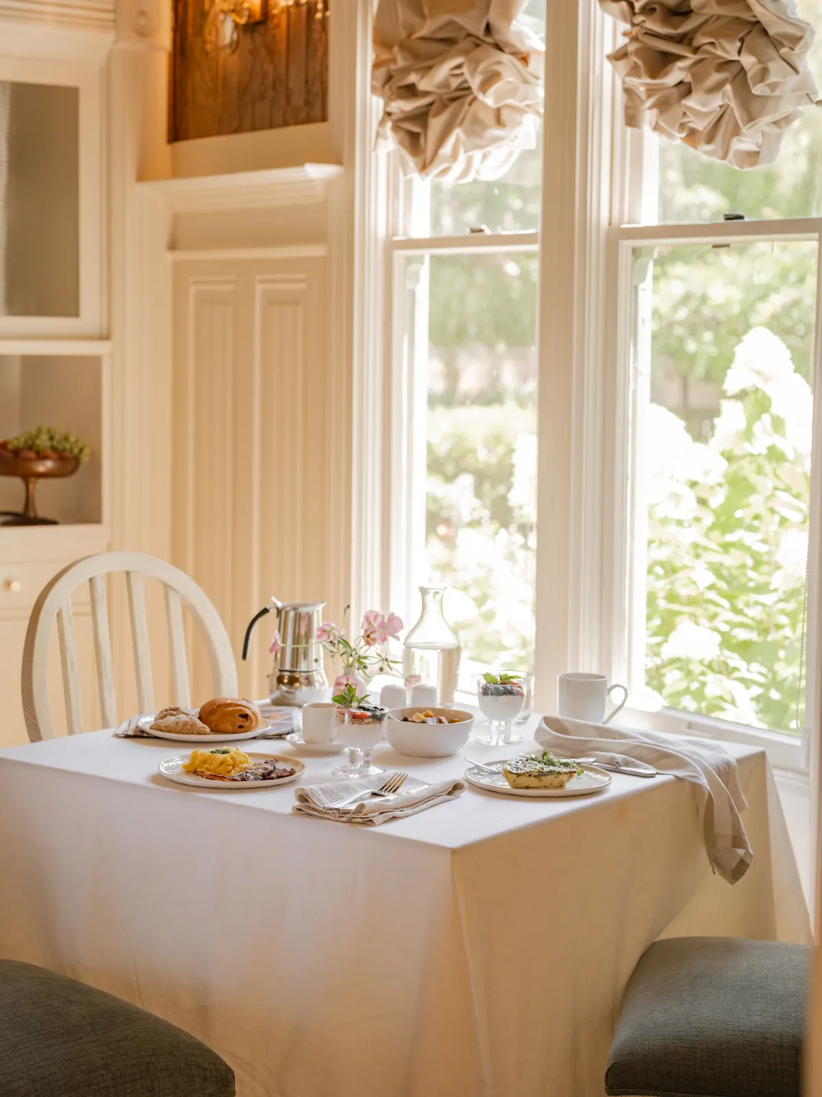 Breakfast table set for two beside a sunlit garden window.