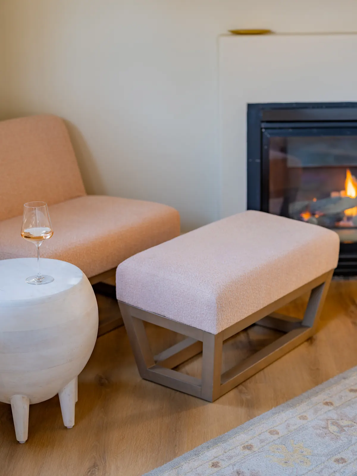 Peach armchair and matching footstool beside a lit fireplace.