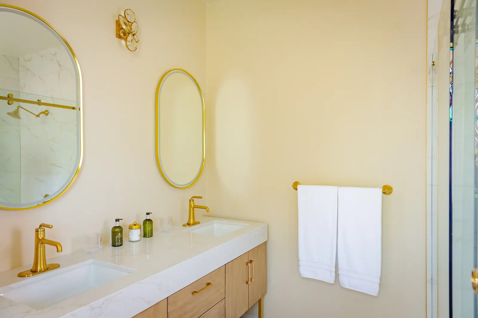 Double bathroom vanity with oval brass mirrors and matching faucets.