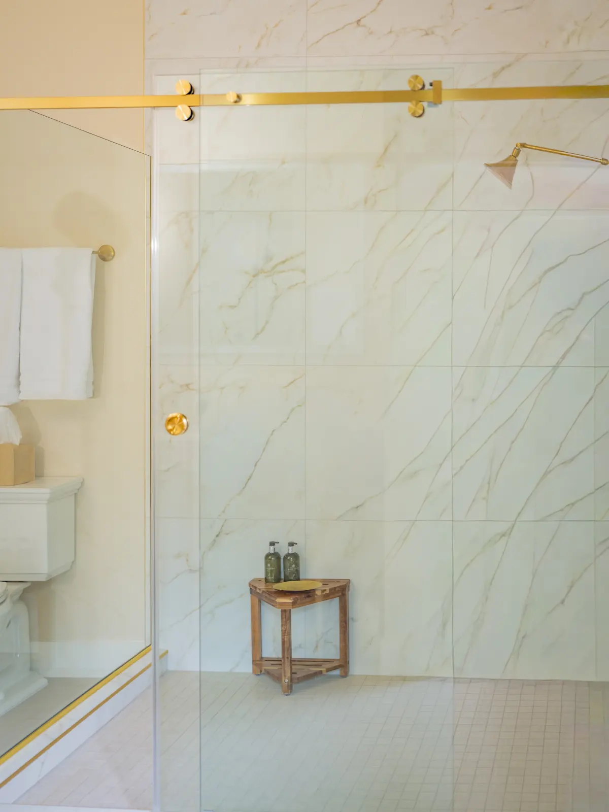 Marble-patterned shower with a glass enclosure and brass fixtures.