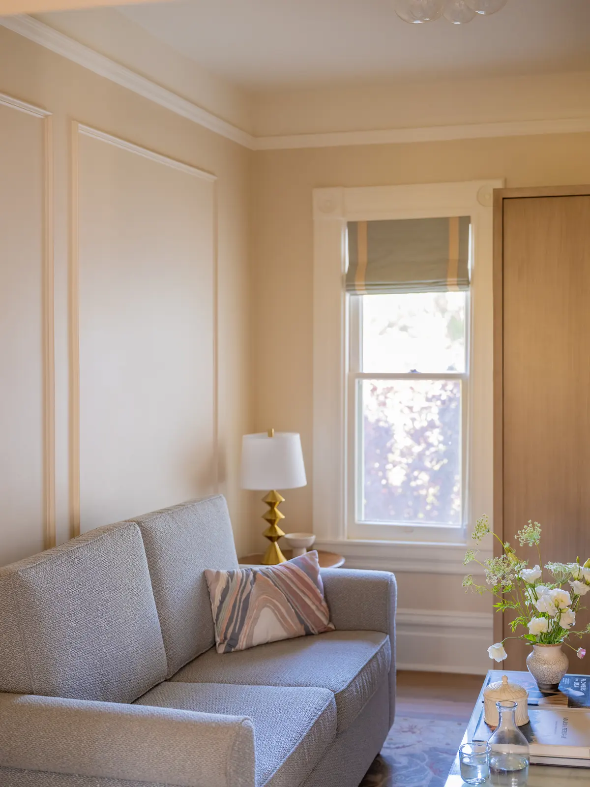 Gray sofa beside a tall window in a sunlit sitting area.