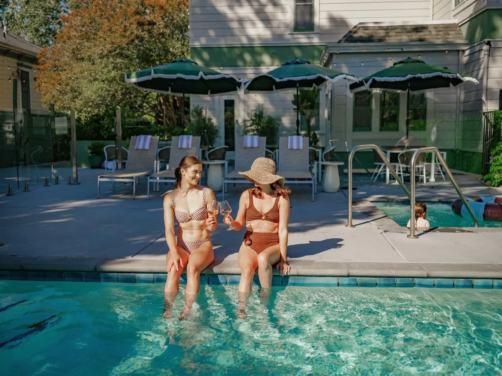 Two guests enjoying the edge of the pool in the afternoon sun